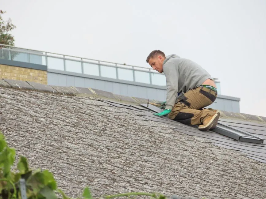 A roofer kneeling on a pitched roof, working along a course beside a rooflight